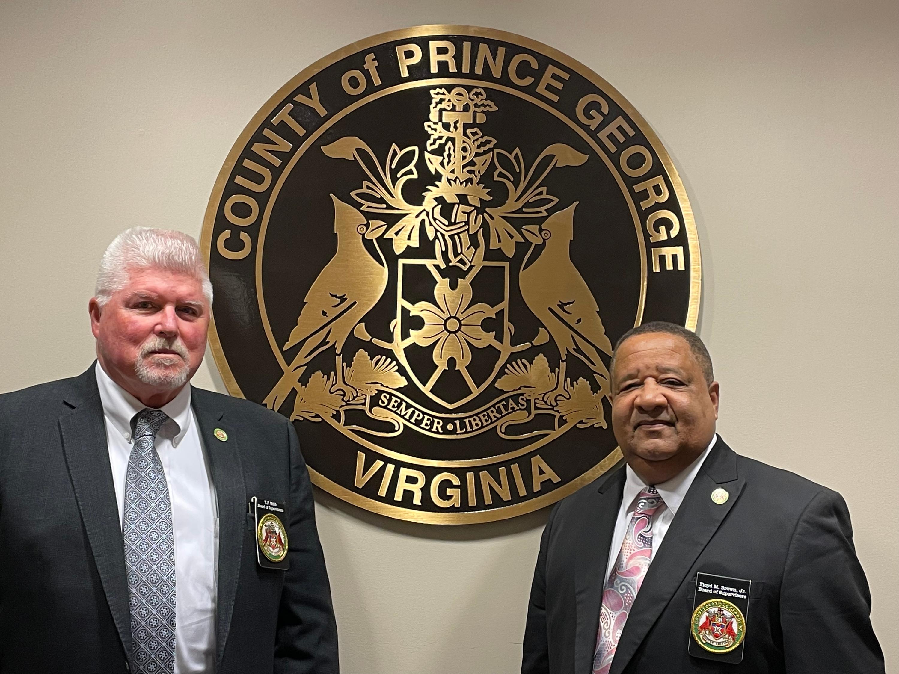 Chairman T.J. Webb and Vice Chairman Floyd Brown are depicted standing in front of the Prince George County Seal. The two gentleman are wearing business suites and standing stoicly.
